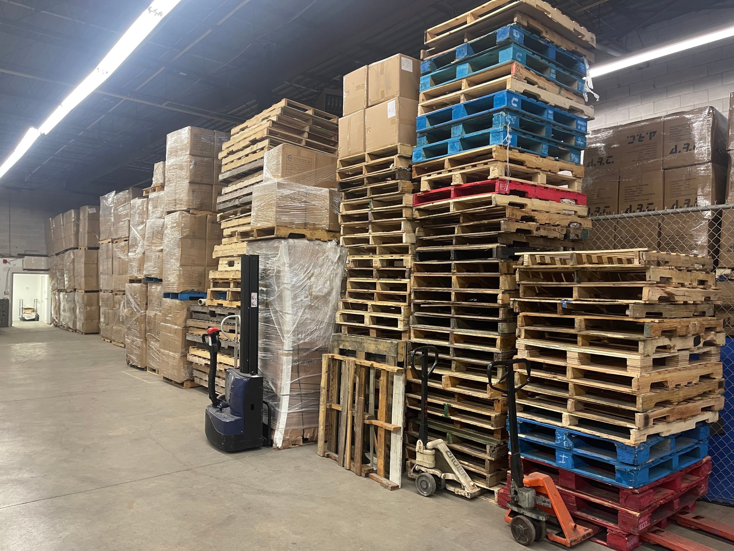 Empty skids stacked by the pallet jacks, with stored goods behind