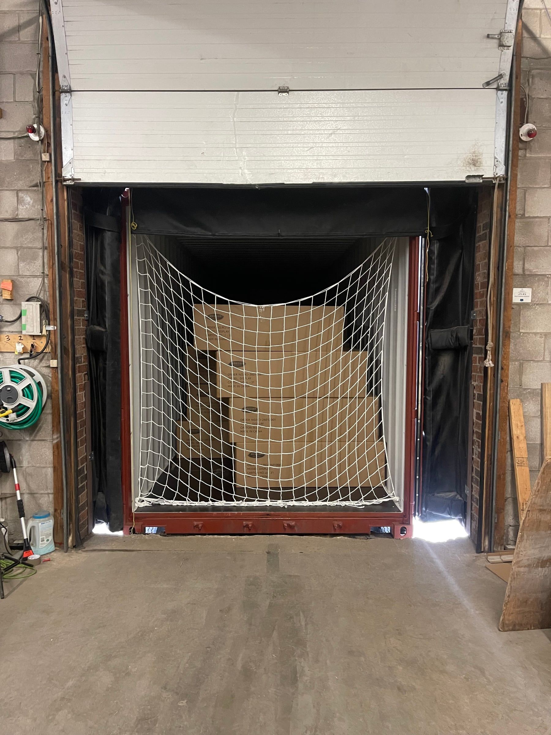 A container backed into our dock door, its load held by a cargo net